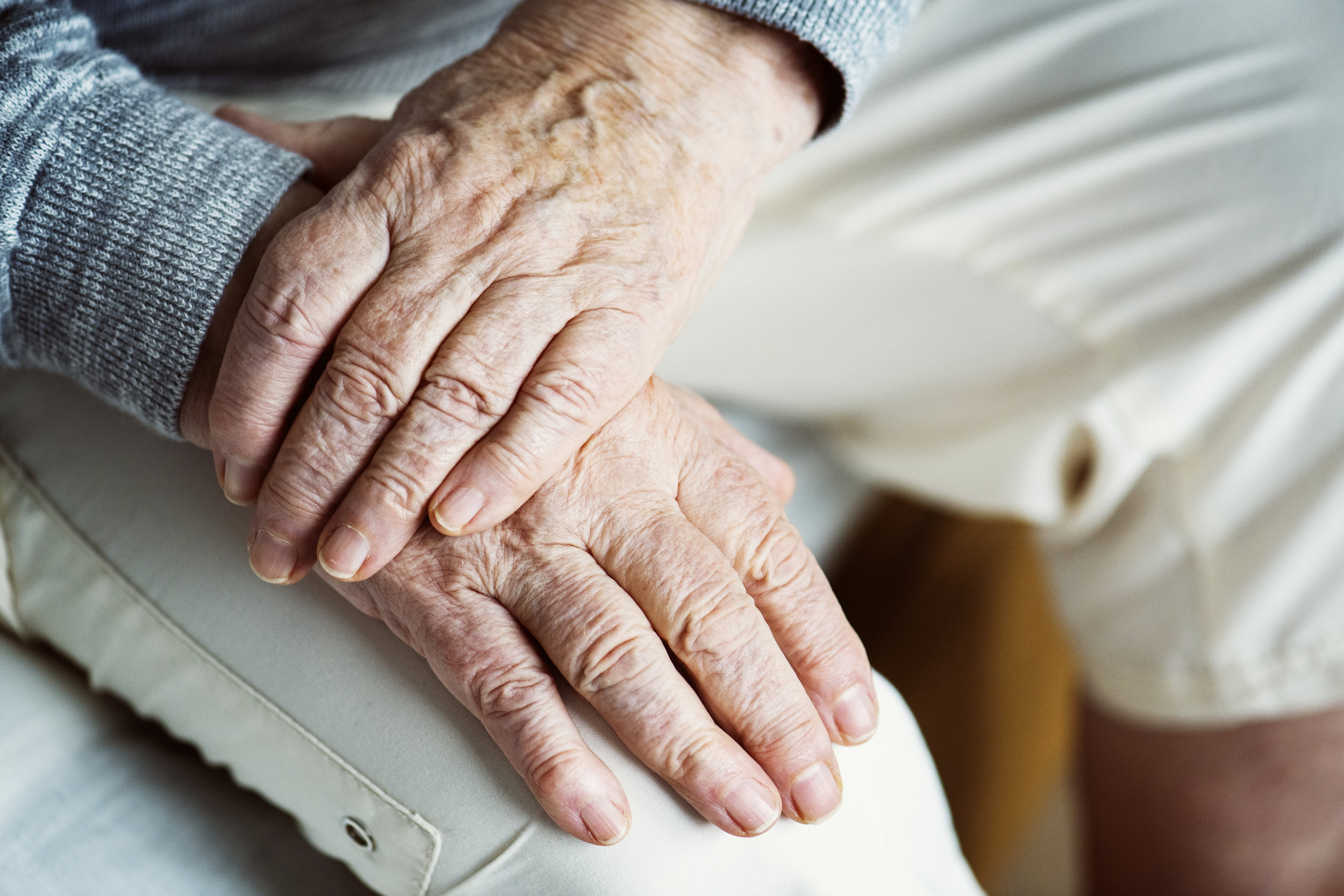 Close-up of elderly person's hands resting on their lap, showing signs of aging and visible wrinkles.